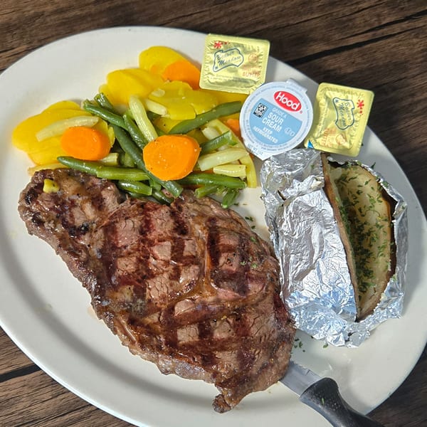 Grilled steak, baked potato, green beans, carrots, and yellow squash on a white plate at Gateway Cafe.