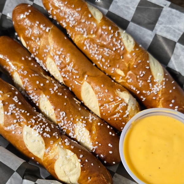 Four salted pretzel sticks with a side of cheese dip in a checkered paper-lined basket.