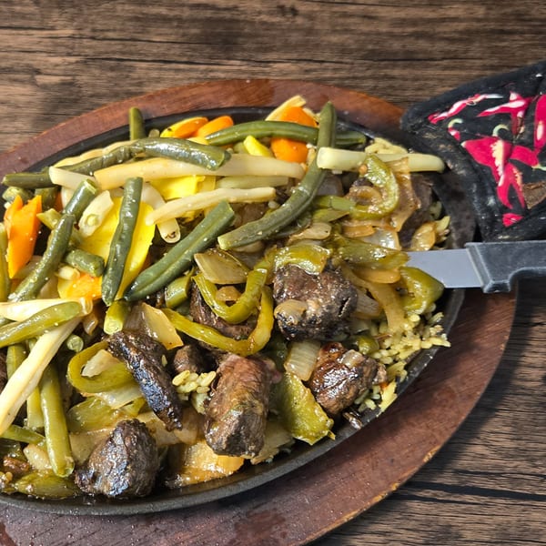 Sizzling steak fajitas with green beans, yellow squash, and bell peppers on a wooden table.
