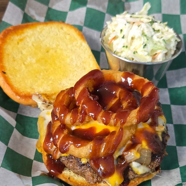 A Gateway Cafe burger with onion rings, BBQ sauce, cheese, and a side of coleslaw.