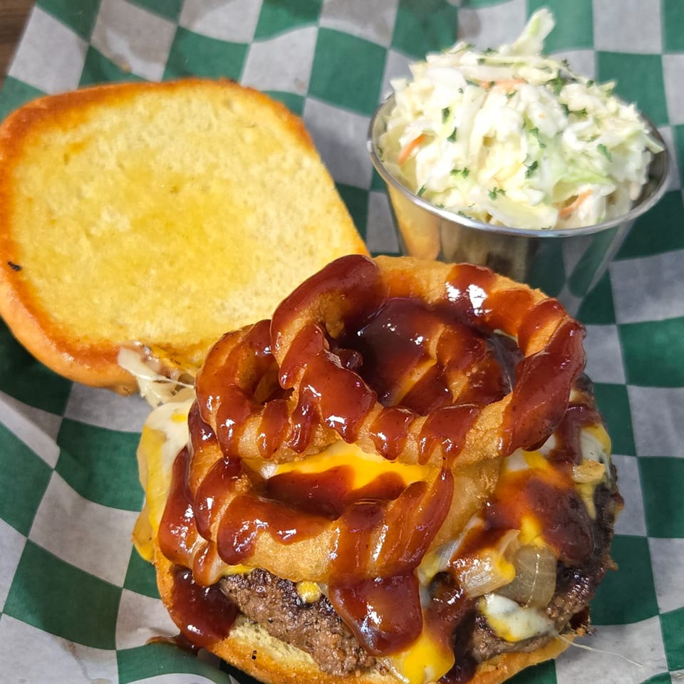 A Gateway Cafe burger with onion rings, BBQ sauce, cheese, and a side of coleslaw.