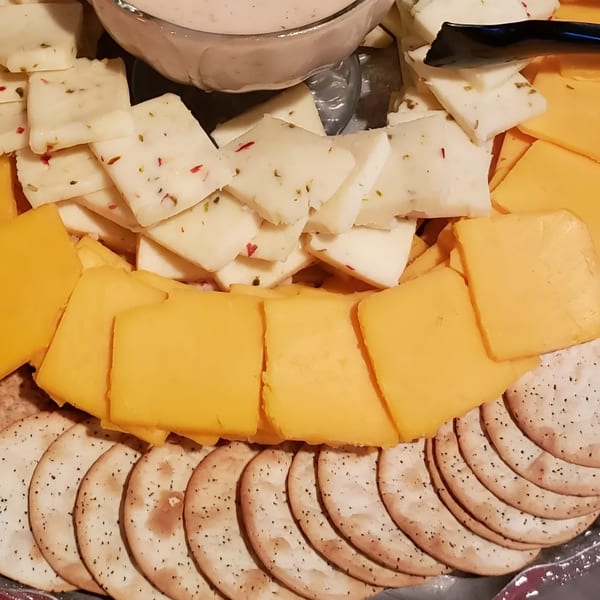 A platter of cheddar and pepper jack cheese slices with crackers and a dip.