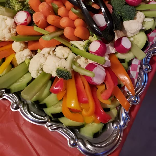 A silver platter overflowing with fresh vegetables including carrots, broccoli, cauliflower, radishes, and bell peppers.