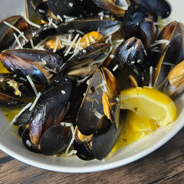 Steamed mussels in a white bowl with a lemon wedge, garlic, and shredded cheese.