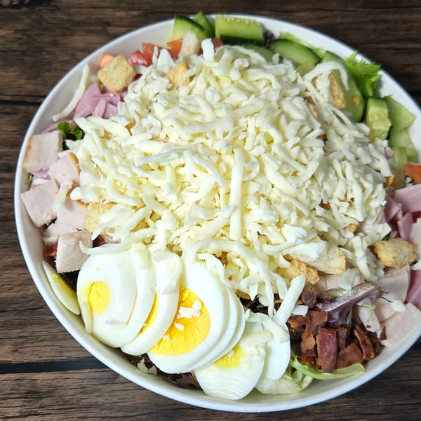 A large Gateway Cafe Cobb salad with shredded cheese, ham, bacon, eggs, and vegetables.