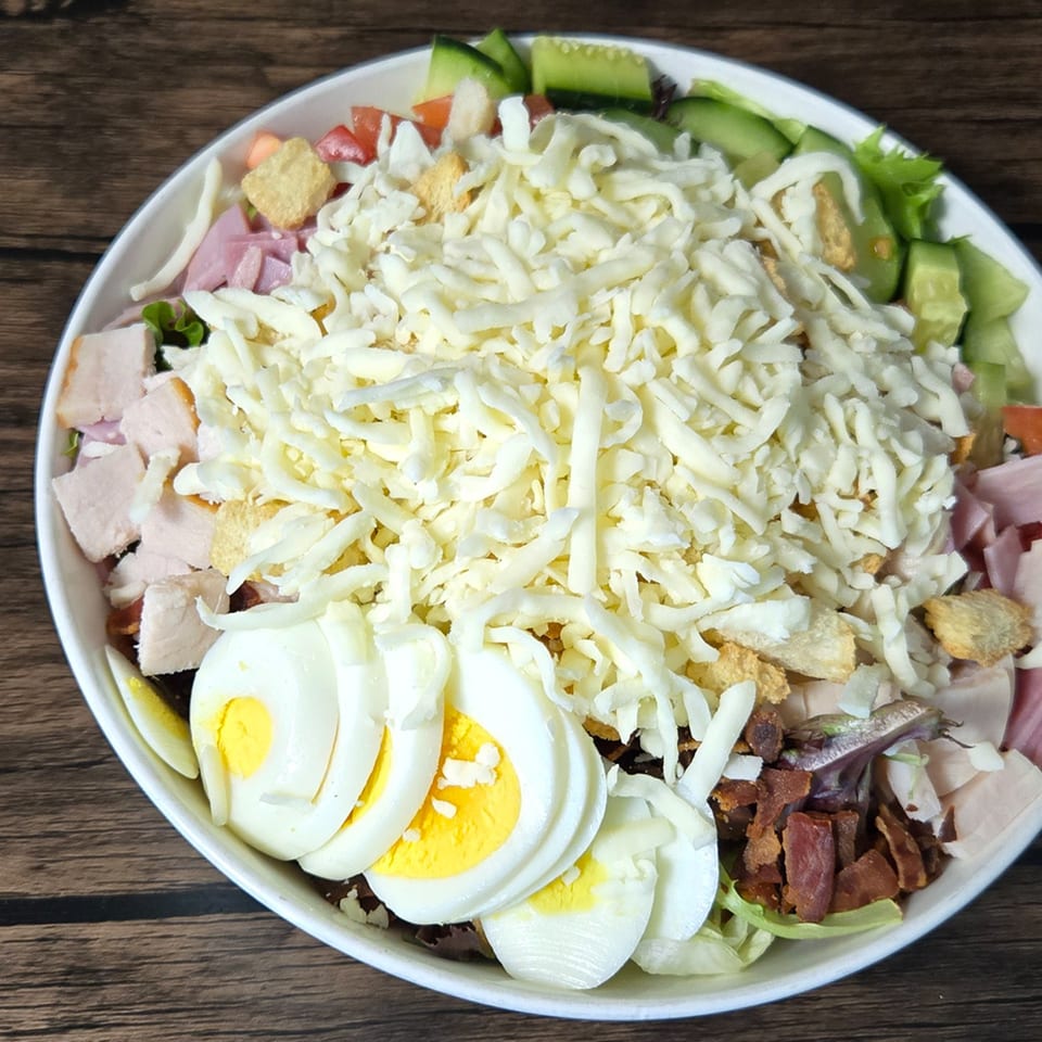 A large Gateway Cafe Cobb salad with shredded cheese, ham, bacon, eggs, and vegetables.